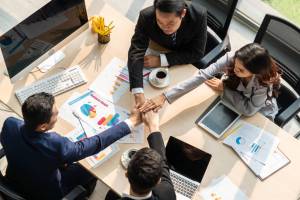 Happy business people celebrate teamwork success together with joy at office table shot from top view . Young businessman and businesswoman workers express cheerful victory showing unity and support .